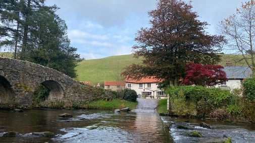 Looking across a ford surround by trees with an old stone bridge on the left hand side